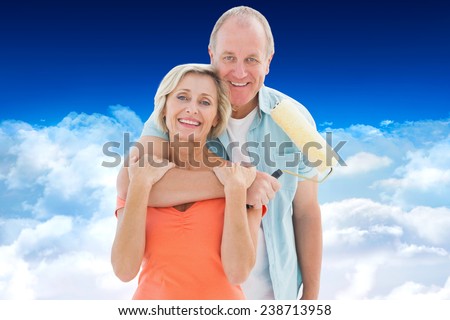 Happy older couple holding paint roller against bright blue sky over clouds