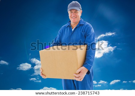 Happy delivery man holding cardboard box against cloudy sky with sunshine