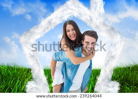 Happy hipster giving his girlfriend a piggy back against field of grass under blue sky