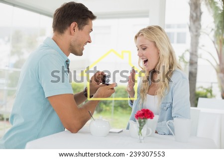 Man proposing marriage to his shocked blonde girlfriend against house outline