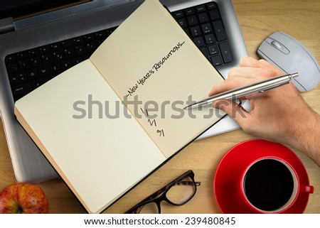 Composite image of hand writing new years resolutions against overhead of laptop with notebook