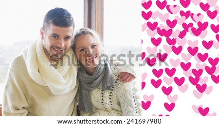 Couple in winter clothing sitting against window against valentines day pattern