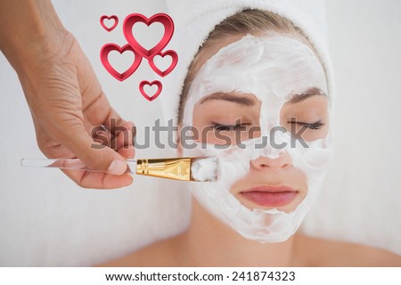 Beautiful blonde getting a facial treatment against pink hearts