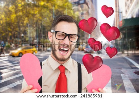 Geeky hipster crying and holding broken heart card against blurry new york street