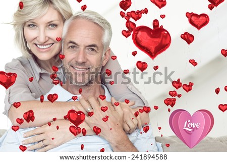 Smiling woman embracing mature man from behind on sofa against love heart