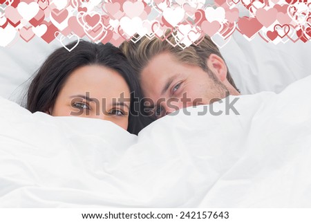 Couple hiding under the duvet against valentines heart design