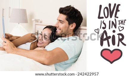 Attractive couple lying in bed with tablet pc against love is in the air