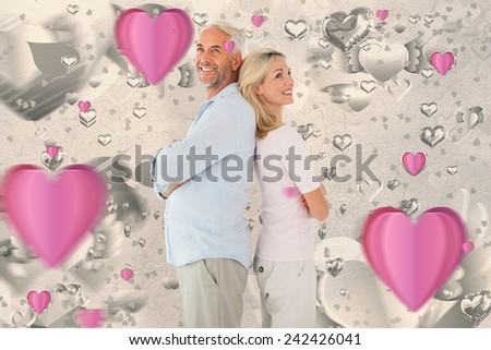 Smiling couple standing leaning backs together against grey valentines heart pattern