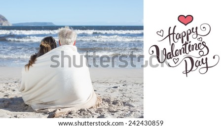 Couple sitting on the beach under blanket looking out to sea against happy valentines day