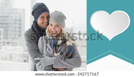 Cute couple in warm clothing smiling at camera against heart label