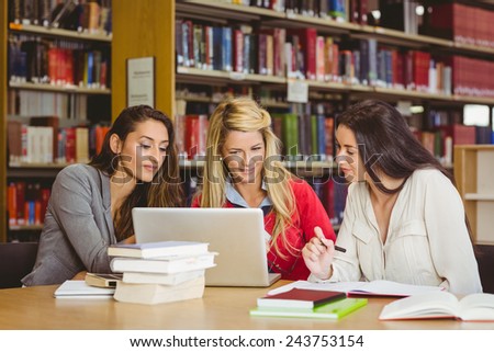 Smiling mature student with classmates using laptop in library