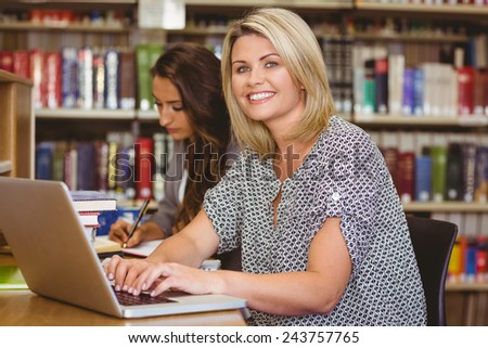Smiling mature female students using her laptop in library