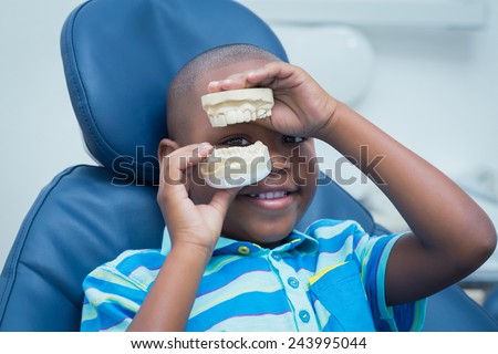 Portrait of smiling young boy holding mouth model in the dentists chair