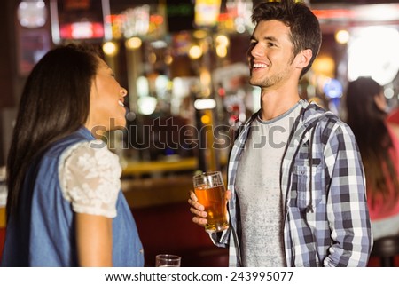 Smiling friends talking and drinking beer and mixed drink in a bar