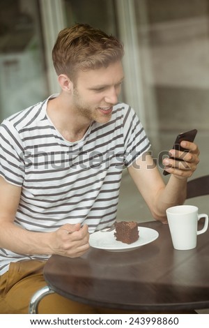Smiling student with chocolate cake using smartphone in cafe at the university