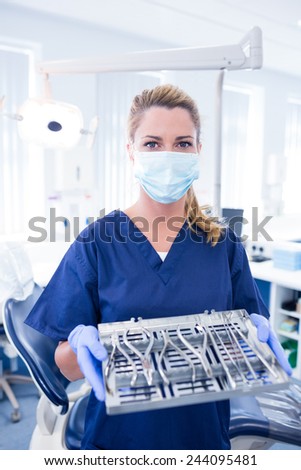Dentist in blue scrubs offering tray of tools at the dental clinic