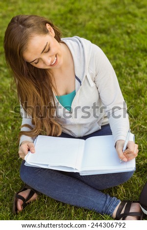 Smiling university student sitting and writing on notepad in park at school