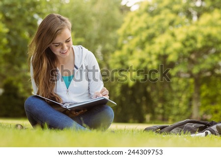 Smiling student sitting and reading book in park at school