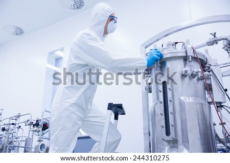 Scientist in protective suit standing on ladder in the factory