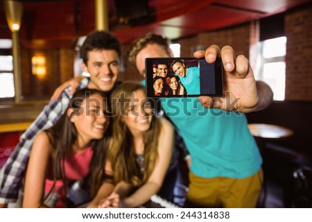 Portrait of happy friends taking a photo with a phone in a bar