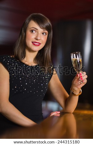 Pretty brunette drinking glass of champagne in a bar