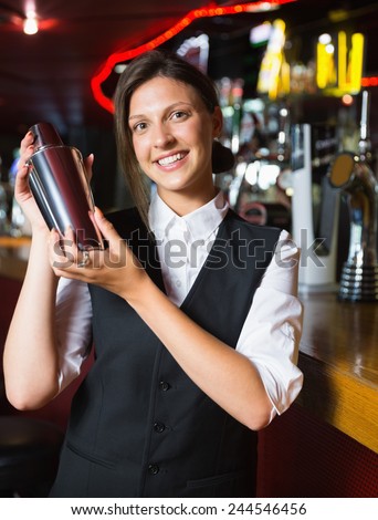Happy barmaid smiling at camera making cocktail in a bar