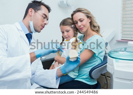 Male dentist with assistant teaching girl how to brush teeth
