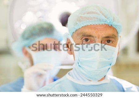 Young surgeon tying older surgeons mask at the university