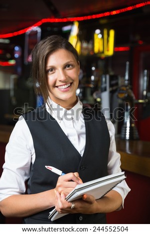 Happy barmaid smiling at camera taking notes in a bar