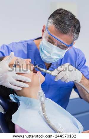 Dentist wearing surgical mask and safety glasses examining a patient