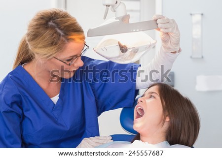 Pediatric dentist examining with a light her young patient in dental clinic