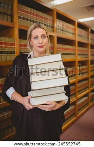 Lawyer holding heavy pile of books standing in library