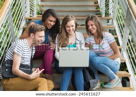 Smiling students sitting on steps with laptop at the university