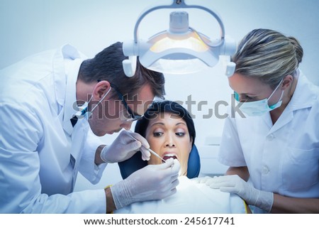 Male dentist with assistant examining womans teeth in the dentists chair