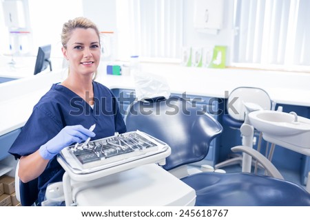 Dentist sitting with tray of tools smiling at camera at the dental clinic