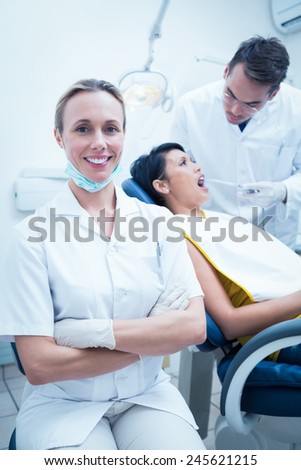 Portrait of smiling female dentist with assistant examining womans teeth in the dentists chair