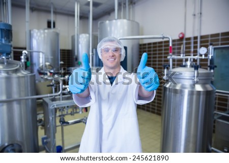 Positive man in lab coat giving thumbs up in the factory