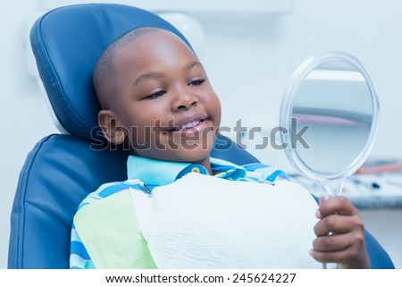 Smiling young boy looking at mirror in the dentists chair