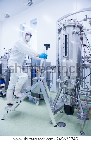 Scientist in protective suit climbing on ladder in the factory