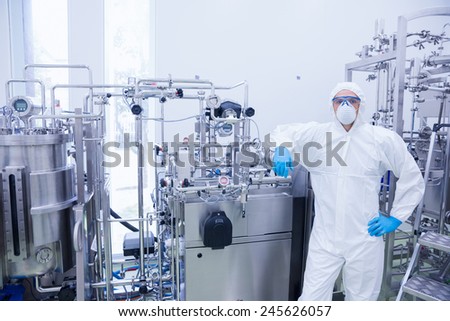 Scientist in protective suit leaning against machine in the factory