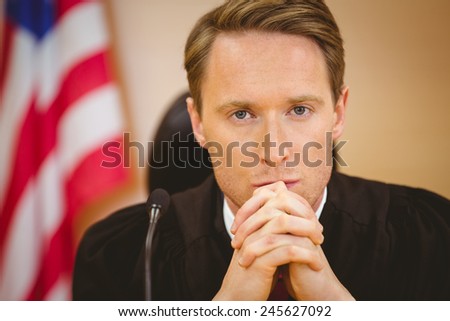 Unsmiling judge with american flag behind him in the court room