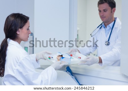 Doctor giving tray with blood sample to his colleague in hospital