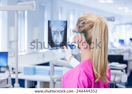 Female dentist in pink scrubs examining x-ray at the dental clinic