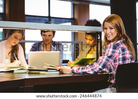 Smiling student sitting at desk looking at camera in library