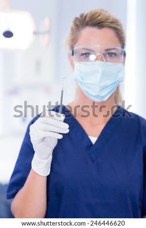 Dentist in mask holding dental explorer at the dental clinic