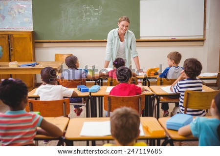 Pretty teacher talking to the young pupils in classroom at the elementary school