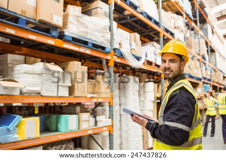 Smiling warehouse manager holding clipboard in a large warehouse