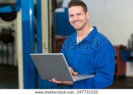 Smiling mechanic using his laptop at the repair garage