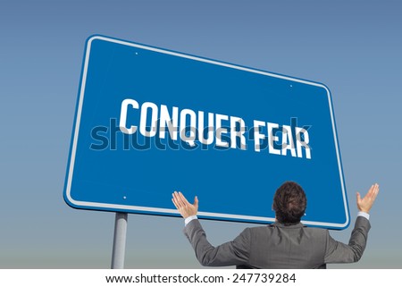 The word conquer fear and businessman posing with arms raised against blue sky