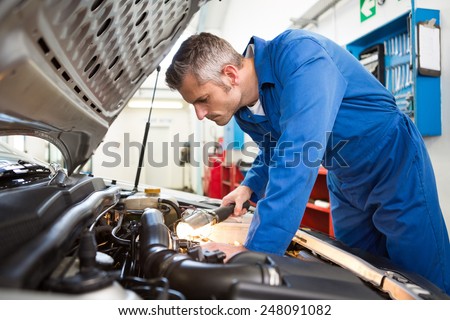 Mechanic examining under hood of car with torch at the repair garage